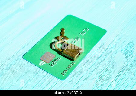 Green credit card secured with padlock and key isolated on a blue wooden background. E-commerce transaction vulnerability concept. Stock Photo