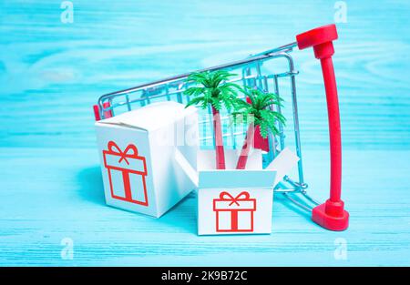 Creative tropical vacation online booking concept: toy shopping cart with gift boxes and palm trees on blue. Stock Photo