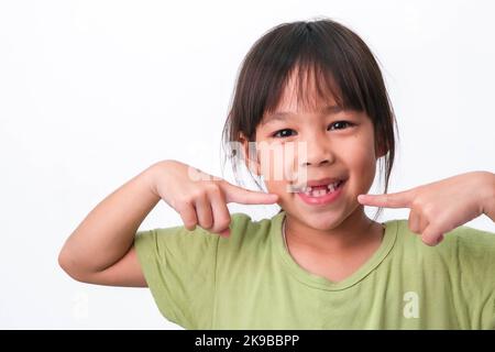 Portrait of an Asian girl with broken upper baby teeth and first permanent teeth. Friendly little girl showing her broken teeth isolated on white back Stock Photo