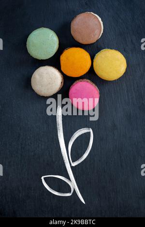 Arrangement of french macarons in the shape of a flower on black slate background, creative food decor concept Stock Photo