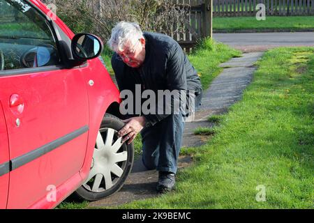 checking tyre tread on a motor vehicle. Man checking depth of his tires with his hands to make sure they are legal. Stock Photo