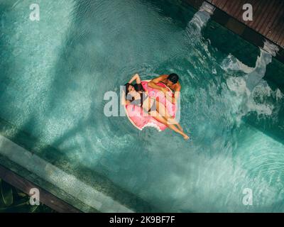 Aerial view of couple enjoying vacation in resort pool. Woman lying on inflatable ring and man in water next to her. Stock Photo