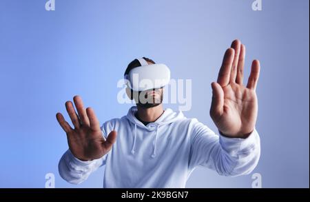 Curious young man touching virtual space with his hands. Young man experiencing a 3D simulation. Young man interacting with the metaverse using virtua Stock Photo