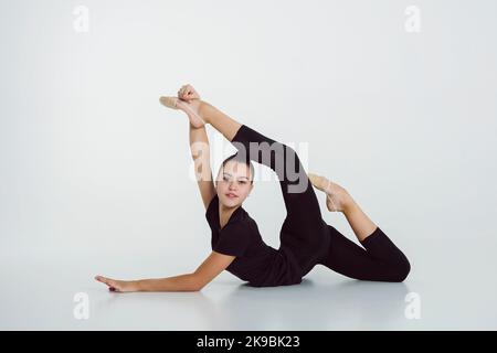 a girl from rhythmic gymnastics in a bodysuit shows stretching lying on the floor Stock Photo