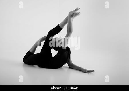 a girl from rhythmic gymnastics in a bodysuit shows stretching lying on the floor Stock Photo