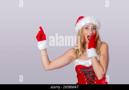 young woman in Santa Claus clothes pointing at something on a white background, Christmas concept. Stock Photo