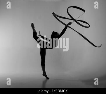 a girl from rhythmic gymnastics in bodysuit shows an exercise with a ribbon Stock Photo