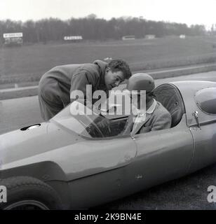 1959, historical, motor racing, racing driving school. Picture shows an male instructor talking to a driver sitting in a Cooper car on the track at the Brands Hatch motor racing circuit, Kent, England, UK. The driver is wearing a sports jacket and helmet and googles of the era. At this time, the Coopers Driving School was based at the race track. Stock Photo