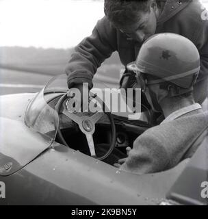 1959, historical, motor racing, racing driving school. Picture shows an male instructor talking to a driver sitting in a Cooper car on the track at the Brands Hatch motor racing circuit, Kent, England, UK. The driver is wearing a sports jacket and helmet and googles of the era. At this time, the Coopers Driving School was based at the race track. Stock Photo