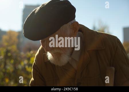 Portrait of old man in garden. Old man on street. Black cap on head of old man. Gray beard. Stock Photo