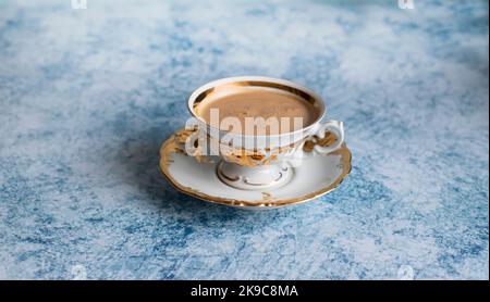 Refined white and gilded coffee cup on an abstract blue background. Coffee with an appetizing golden foam. Stock Photo