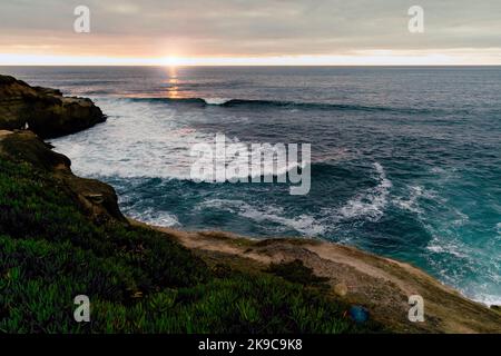 Stunning sunset photo taken in La Jolla, California showing cliffs, waves, and a cove. Landscape sunset photography with greens, blues and oranges. Stock Photo