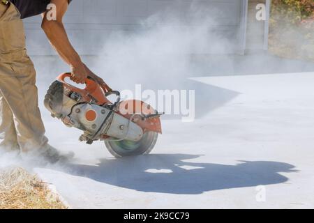 Construction worker cuts with working diamond bladed cut off saw to concrete paving sidewalk Stock Photo