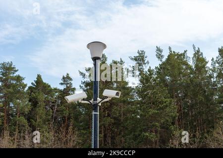 Surveillance cameras mounted on a lamppost at the side of a forest road. security cctv camera. Security in the city. Hidden filming of what is happeni Stock Photo