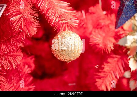 Golden baubles glowing and hanging on decorated red christmas tree. Christmas background Stock Photo