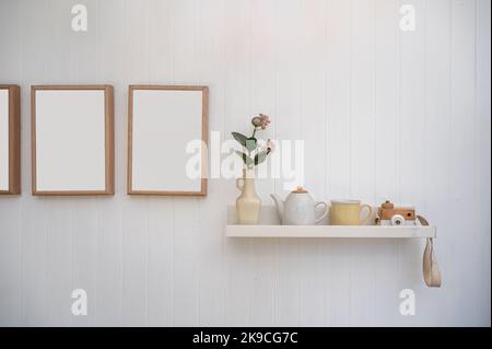 Minimalist of living room interior with flower in vase, ceramic pot, cup, camera mockup and empty wooden picture frame on white wooden wall Stock Photo
