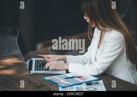 Young Asian Businesswoman working on laptop computer with financial graphs charts , using business account software for data analysis and project mana Stock Photo