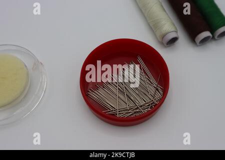 Sewing accessories on a white background. Pins in a circular plastic box, threads Stock Photo