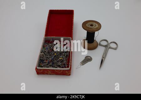 Sewing accessories on a white background. Pins in a box, thread on wooden holder, needle threader and metal scissors Stock Photo