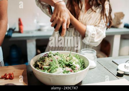 Female hand pouring olive oil on the fresh vegetables salad Stock Photo