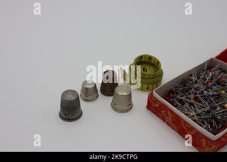 Sewing accessories on a white background. Thimbles, measure tape and a red box with pins Stock Photo