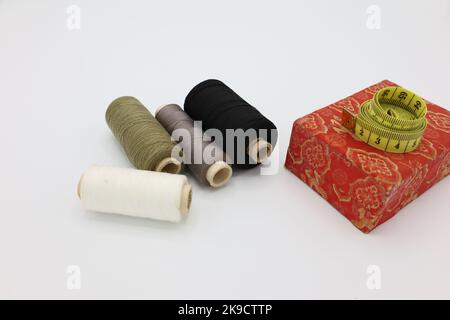 Sewing accessories and tools. Red sewing threads, black scissors, yellow  measuring tape and thimble on a white background. Stock Photo