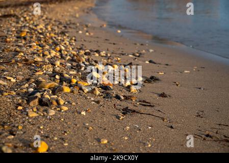 Close-Up Of Sandy Beach With Large Stones Of Ionian Sea In Moraitika, Corfu, Greece At Sunrise. The Coast is Washed by Water.  Stock Photo