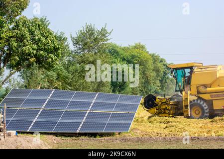 Solar panels for irrigation on the farmland on the other side Combine machine is harvesting the rice crop Stock Photo