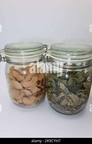 Glass jar filled with dry lemon balm (Melissa officinalis) leaves on a white background and another jar filled with dried, dehydrated apple slices Stock Photo