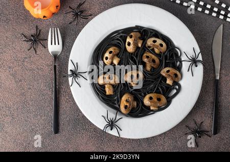 Black Italian spaghetti and mushrooms in form of skulls, idea of cooking vegetarian food for Halloween, Top view Stock Photo