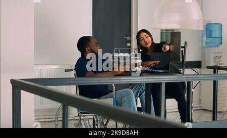 Diverse programmers collaborating on coding project compiling algorithm for new cloud computing user interface. Engineer with impairment in wheelchair working with coder on server. Stock Photo