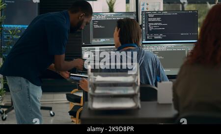 Diverse team of data programers analyzing code programming on laptop and monitor in it agency office. Programmers doing teamwork looking at system network algorithms, coding script. Stock Photo