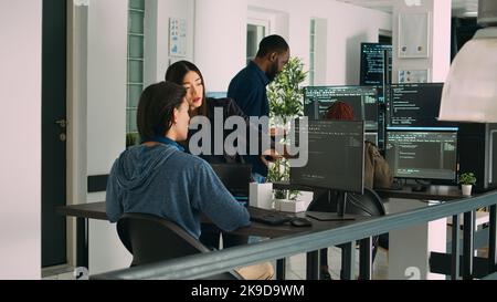 Asian team of artificial intelligence cloud programers talking about programming in it agency office. Compiling code on terminal window server, doing teamwork on developing algorithms. Stock Photo