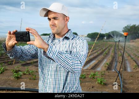 Interested farmer taking photo on smartphone in farm field Stock Photo