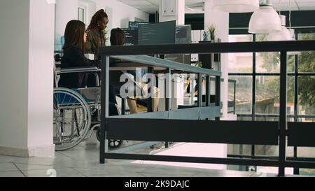 Programer with chronic disability typing source code on computer, working with cloud computing terminal window. Software engineer in wheelchair writing ai algorithm in it company office. Tripod shot. Stock Photo