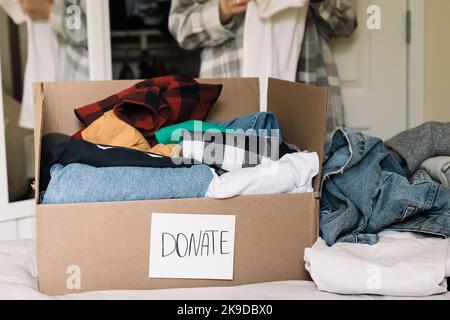 Cardboard box full of clothes to donate. Sorting clothes from the wardrobe, donating, reuse Stock Photo