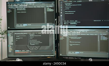 Desk with multiple monitors displaying terminal window and artificial intelligence programming code. Empty software developing agency office with servers cloud computing, html script. Stock Photo
