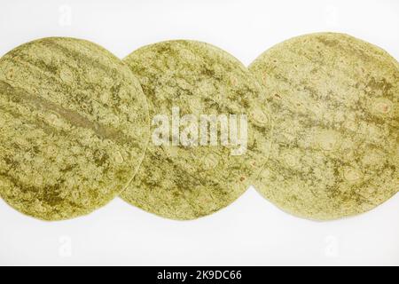 Spinach flavored wheat tortilla wraps on white background. Spanish or Mexican circular unleavened flatbread from wheat flour. Ingredient for cooking fast food or snack. Closeup, texture background Stock Photo