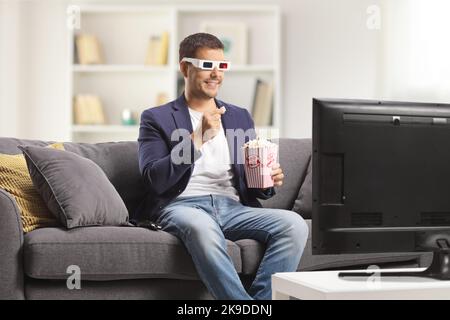 Man with 3d glasses eating popcorn and sitting on a sofa at home watching tv Stock Photo