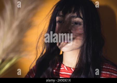 Close-up portrait of young white brunette woman standing in shade spotlit with shadow of plant on her face smiling. Creative portrait photography. Horizontal studio shot. High quality photo Stock Photo