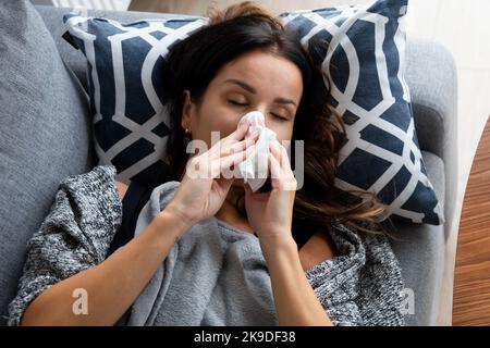 Sick woman blows her nose into a handkerchief, lying on bed Stock Photo
