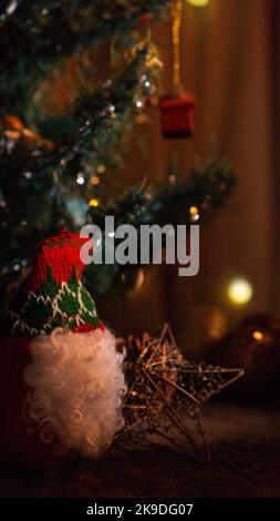 santa claus ornament dances next to a christmas tree and christmas decoration among eucalyptus leaves on a sunny window inside a home interior Stock Photo