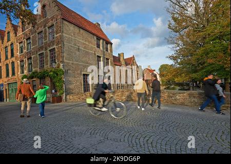 Pedestrians and cyclists on Meestraat in Bruges (Brugge) , Flanders, Belgium, with a typical cobbled street and bridge over the Groenerei Canal. Stock Photo