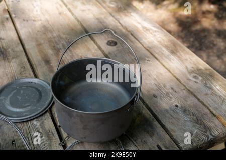 A titanium pot for making food on a gas stove on a camping wooden table in the forest. Stock Photo