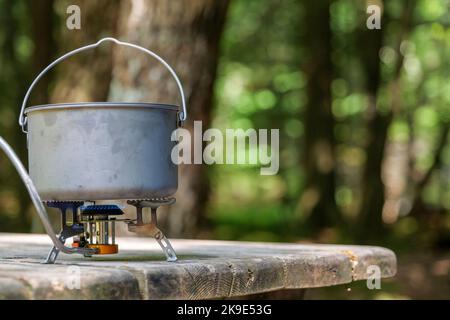 A titanium pot for making food on a gas stove on a camping wooden table in the forest. Stock Photo