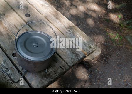 A titanium pot for making food on a gas stove on a camping wooden table in the forest. Stock Photo