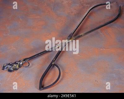 Metal tongs for coals as fireplace accessories on a grunge rusty background Stock Photo
