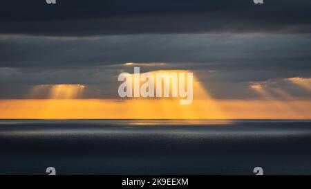 Crepuscular light rays shining through clouds over the ocean Stock Photo