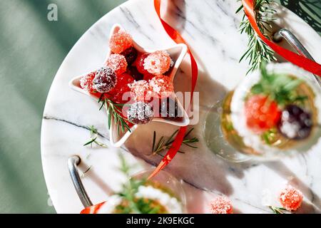 Christmas sweets in white plate a shape of star near wine glasses with cocktail with sparkling wine, rosemary and cherry, top view. Winter xmas and ne Stock Photo