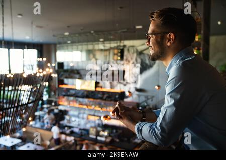 Happy businessman, restaurant owner proudly looking at crowded restaurant Stock Photo